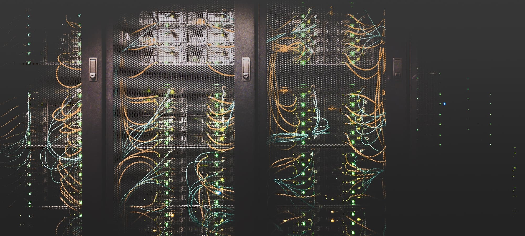 Server racks behind mesh doors, patched with amber and teal cabling.